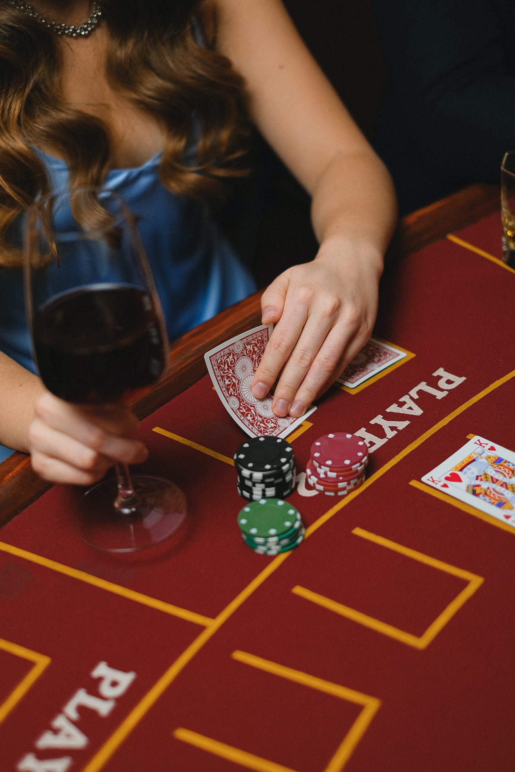 woman in the act of peeking at her cards while holding a glass of wine, cards and chips on casino table