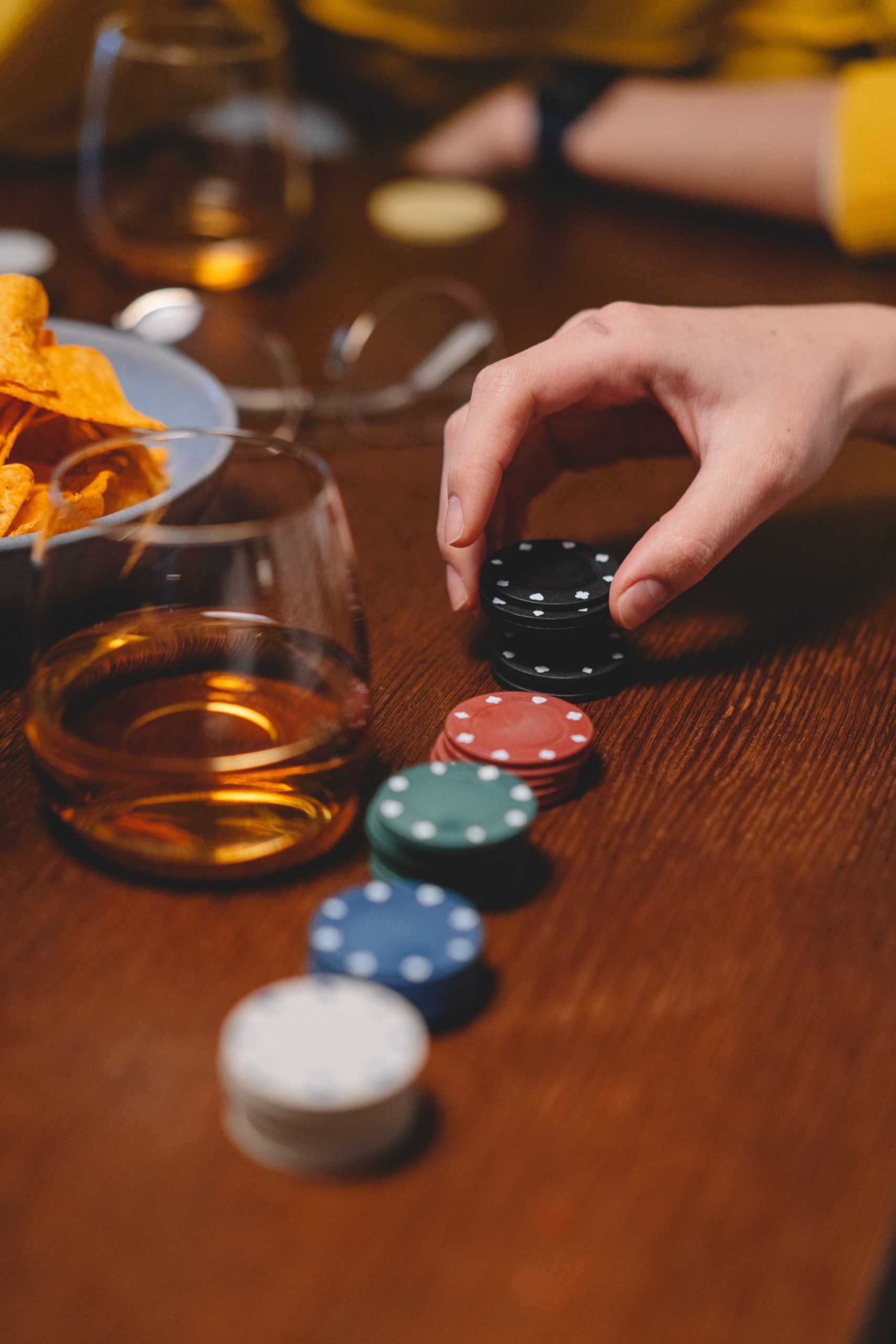 person holding poker chips, casino chips aligned in a row on a wooden table