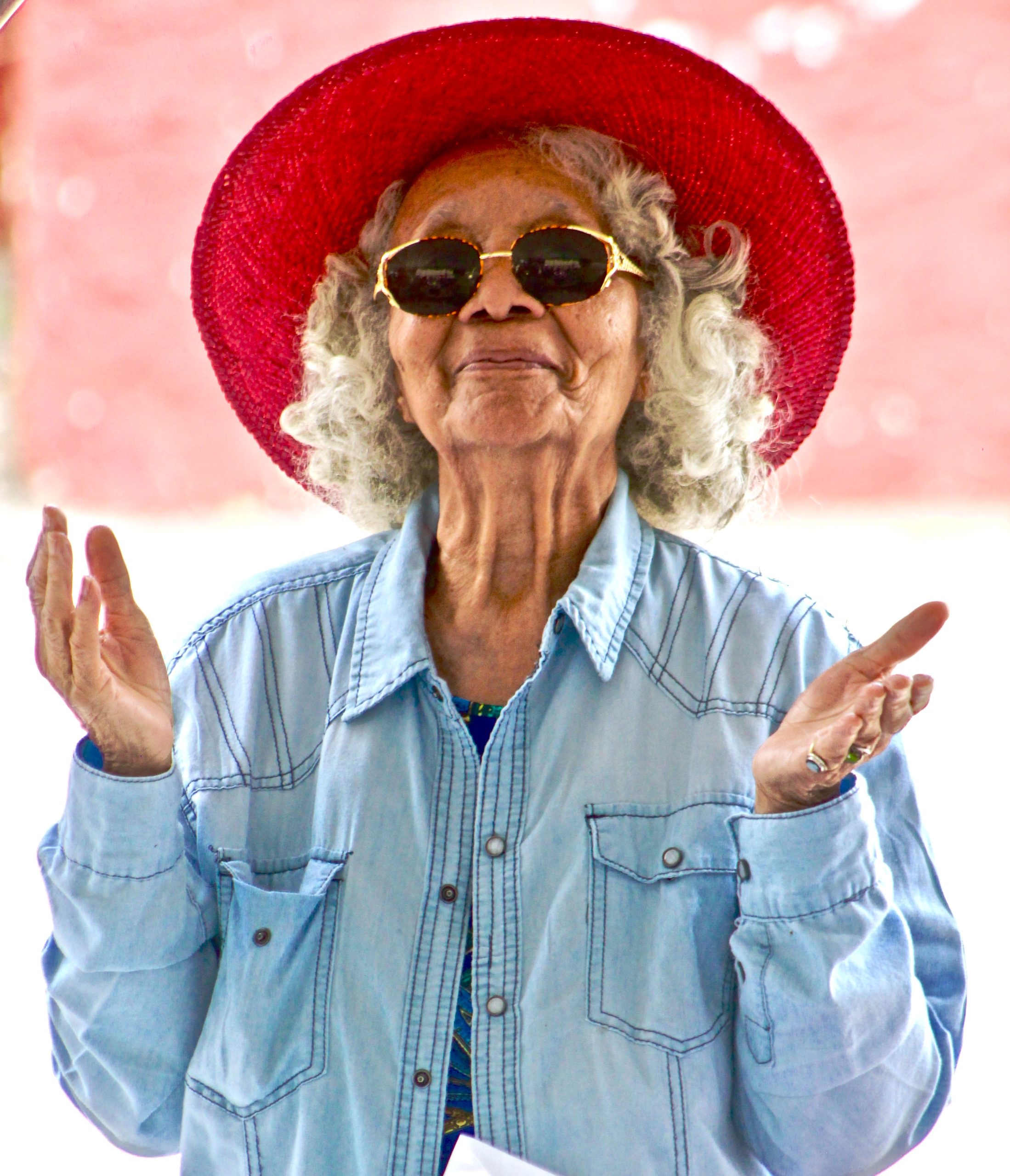 old woman wearing red hat and shades with palms facing upwards